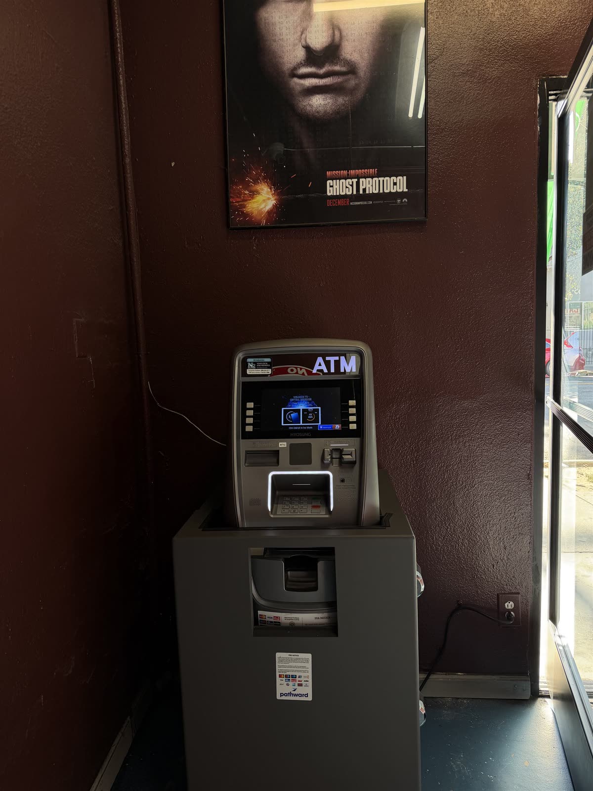 The ATM standing inside the shop against a dark red wall.
